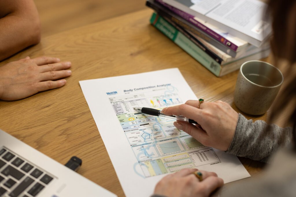 Zdjęcie przedstawia omawianie wydruku analizy składu ciała. Dietetyk omawia parametry pacjenta w celu optymalizacji żywienia.
