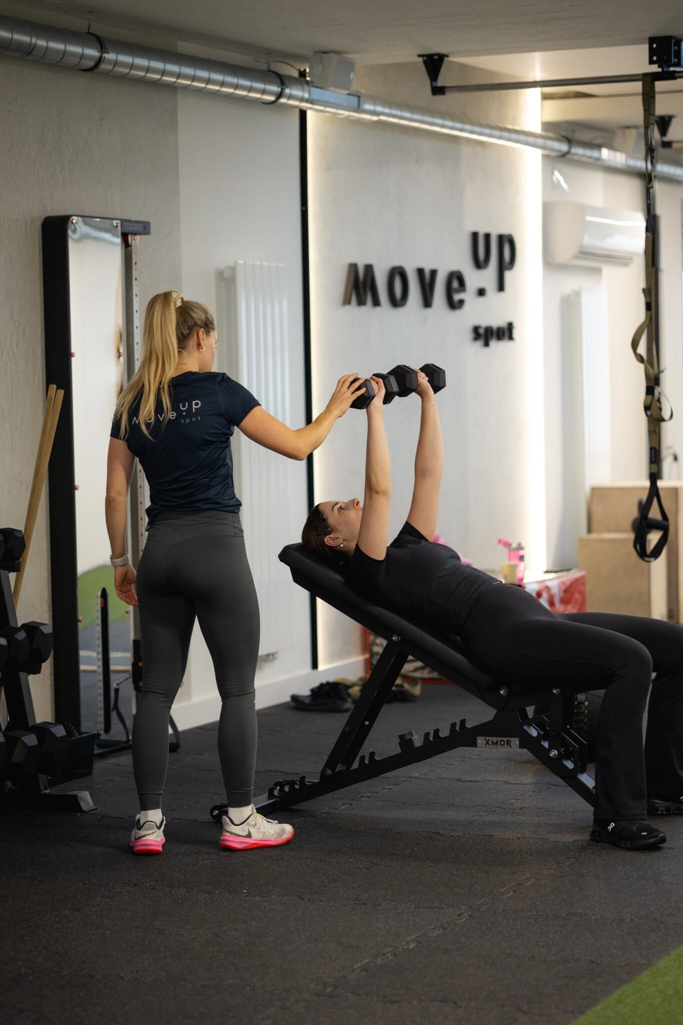 Trenerka personalna korygująca klientkę podczas wyciskania na ławeczce. Widać przestrzeń kameralnego studia treningowego w Poznaniu, czysta, z dbałością o szczegóły.